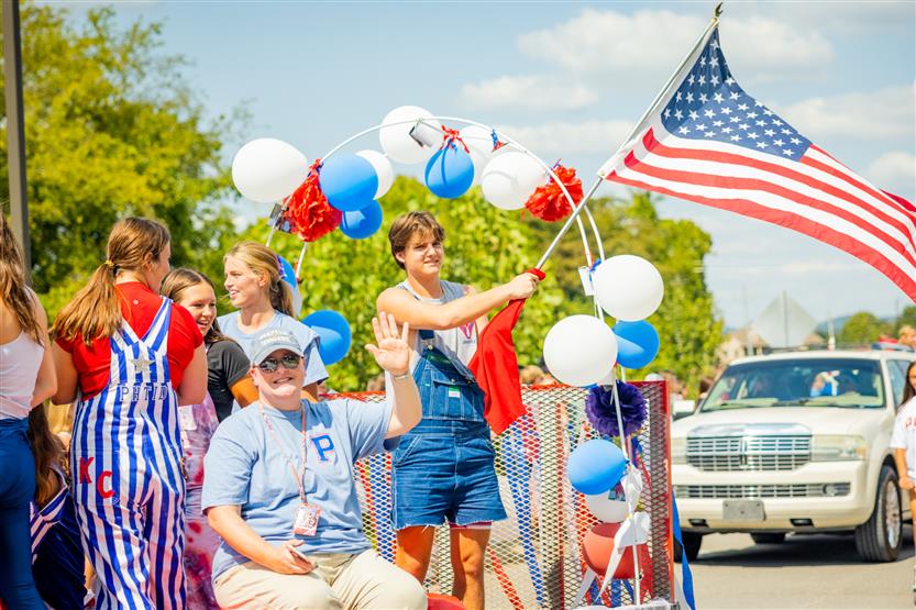 Students sit on a homecoming float while waving a flag